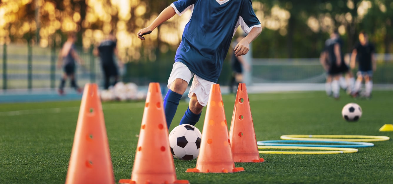 Soccer Boy on Training with Ball and Soccer Cones. Dribbling Drill. Soccer Kids Dribble Training. Youth Soccer Club Practice Session. Boys in Sports Team in Red Soccer Uniforms